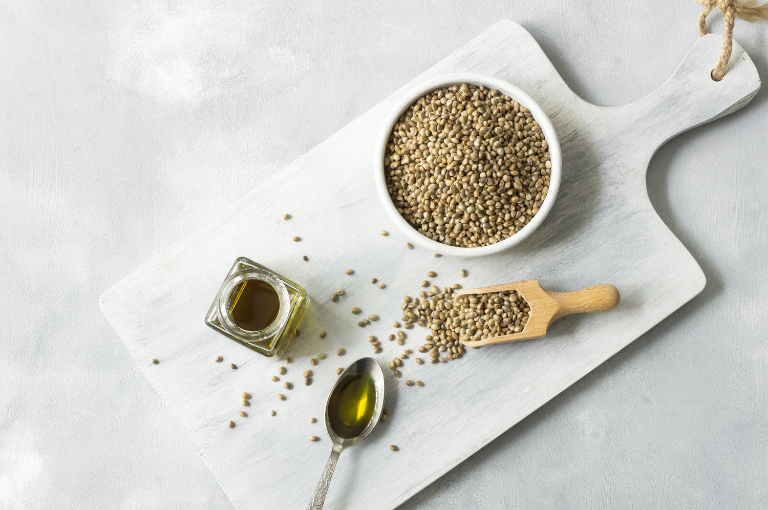 Hulled seeds in a bowl with a jar of oil, spoon, and wooden scoop on a marble surface.